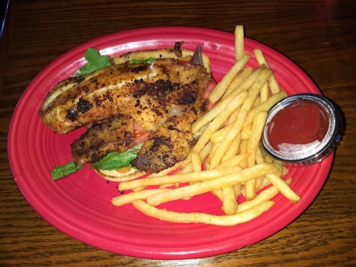 A red plate with crispy fish fillets on lettuce and tomato, served with French fries and a small cup of ketchup.
