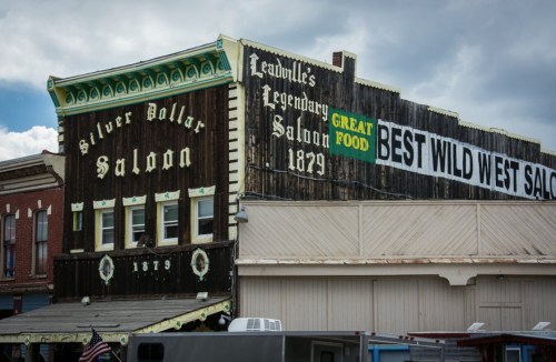 Historic building with "Silver Dollar Saloon" and "Best Wild West Saloon" signs, set against a cloudy sky.