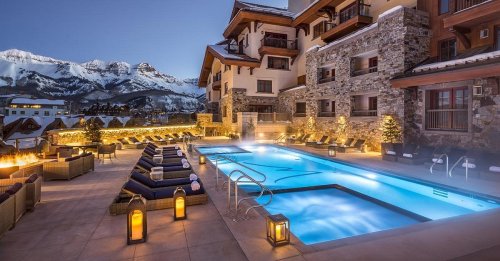 A luxurious pool area with mountain views, cozy seating, and glowing lanterns, set against a twilight sky.