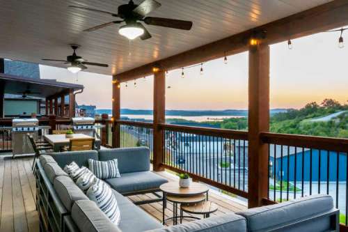 A cozy outdoor patio with a sectional sofa, table, and string lights, overlooking a sunset by the water.