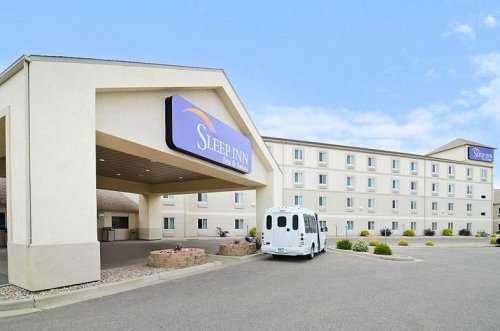 Exterior view of a Sleep Inn hotel with a white shuttle van parked in front and a clear blue sky.