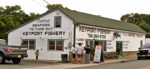 A seafood takeout shop with a white exterior, featuring signs for Keyport Fishery and people outside.