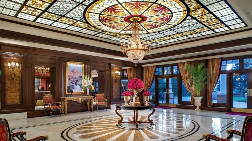 Luxurious lobby with a stained glass ceiling, elegant chandelier, floral arrangements, and ornate furnishings.