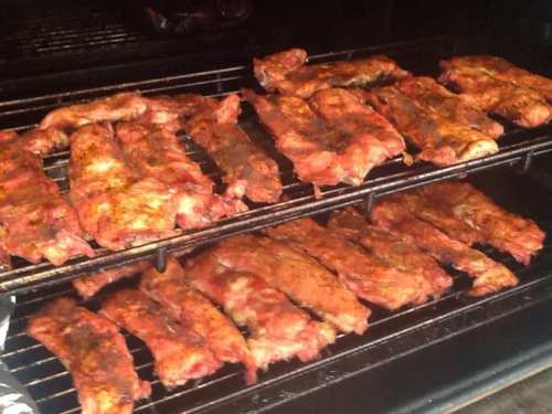 Grilled ribs cooking on a smoker, seasoned and arranged on metal racks.