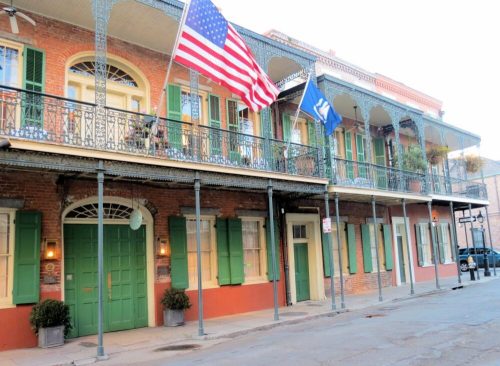 Historic building with green shutters, American and state flags, and wrought iron balconies in a charming street setting.