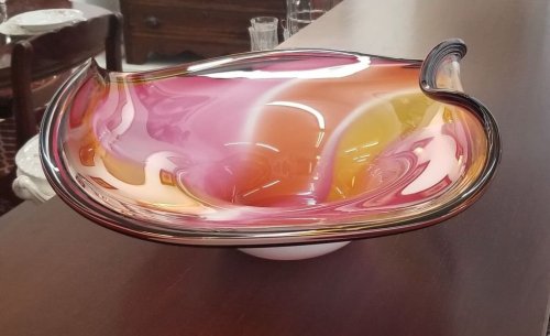 A colorful, swirled glass bowl with shades of pink, orange, and yellow, resting on a wooden surface.