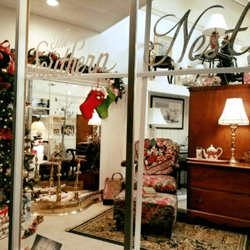 A cozy holiday-themed room with a Christmas tree, stockings, and festive decorations, featuring a chair and lamp.
