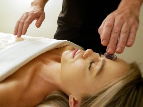 A person receiving a facial treatment with a crystal on their forehead, eyes closed, relaxing on a treatment table.