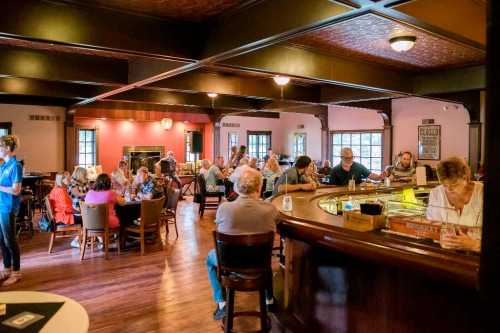 A lively restaurant scene with diners at tables and a bar, featuring warm lighting and a cozy atmosphere.