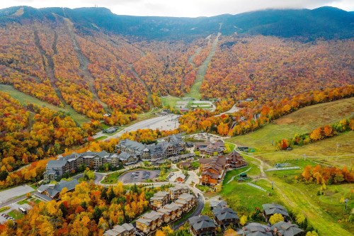 Aerial view of a resort nestled in vibrant autumn foliage, surrounded by mountains and ski slopes.