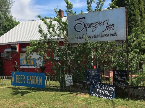 Sign for Squeeze Inn with "Open" and various offerings, including beer garden, live music, and vacation rentals.