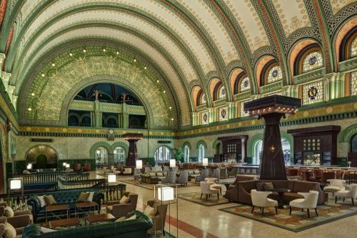 Elegant interior of a grand hall featuring ornate green and gold decor, arched ceilings, and stylish seating areas.