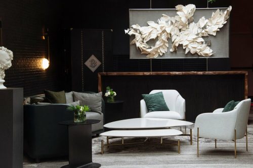 A stylish lounge area featuring modern furniture, decorative plants, and a large leaf art piece on the wall.