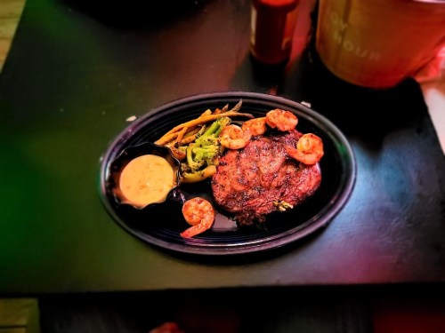 A plate featuring grilled steak, shrimp, and mixed vegetables with a dipping sauce on the side.