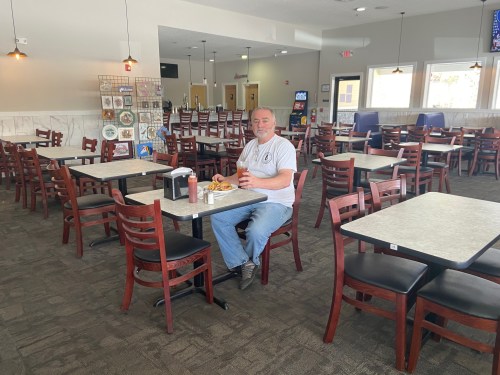 A man sits alone at a table in a nearly empty restaurant, enjoying a meal with various condiments nearby.