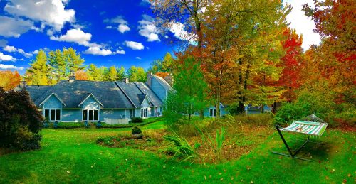 A serene landscape featuring a cozy house surrounded by vibrant autumn trees and a hammock in a lush green yard.