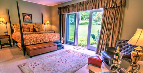 Cozy bedroom with a four-poster bed, elegant decor, and large windows overlooking a garden.
