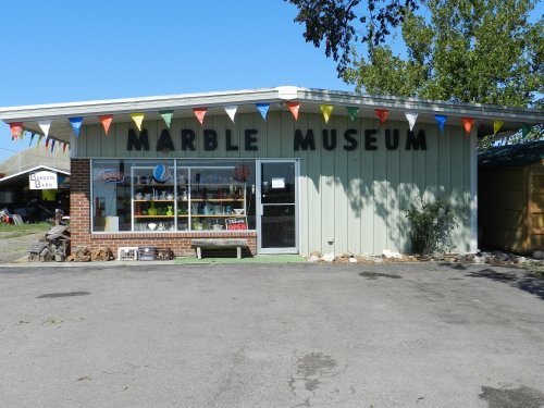 Exterior of the Marble Museum, featuring colorful flags, a display window, and a clear blue sky.