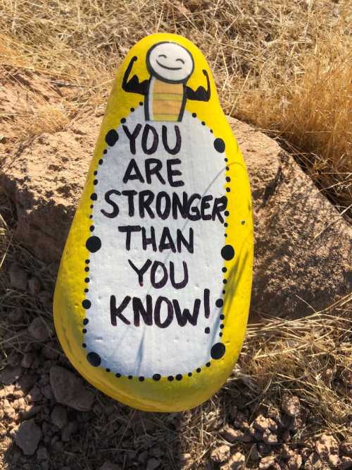 A painted yellow rock with the message "You are stronger than you know!" and a smiling character with muscles.