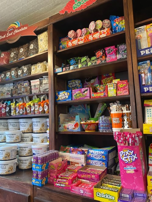 A colorful display of various candies and snacks on wooden shelves in a shop.