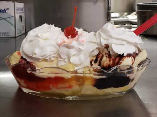 A banana split with three scoops of ice cream, topped with whipped cream and cherries, served in a glass dish.