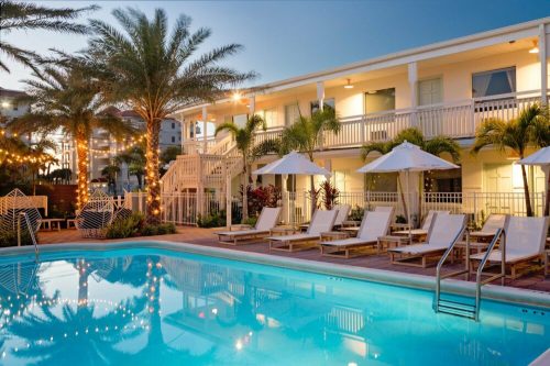 A serene pool area with lounge chairs, palm trees, and illuminated buildings at dusk.
