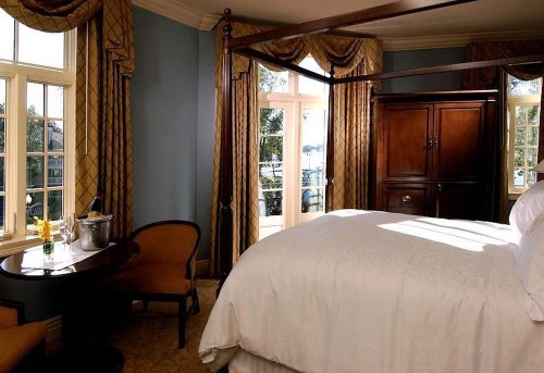 Cozy hotel room with a four-poster bed, elegant curtains, a wooden wardrobe, and a small table by the window.