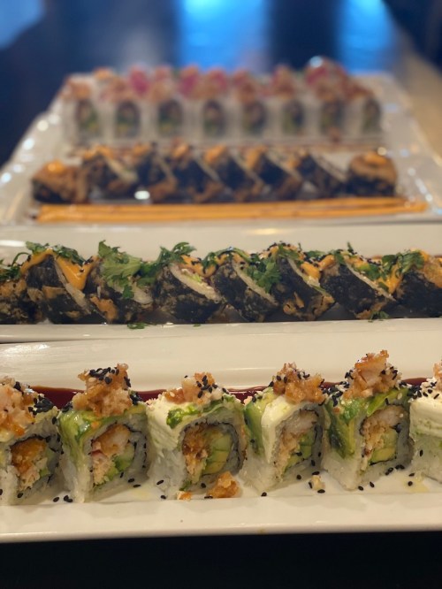 A variety of sushi rolls arranged on a white platter, featuring colorful ingredients and garnishes.