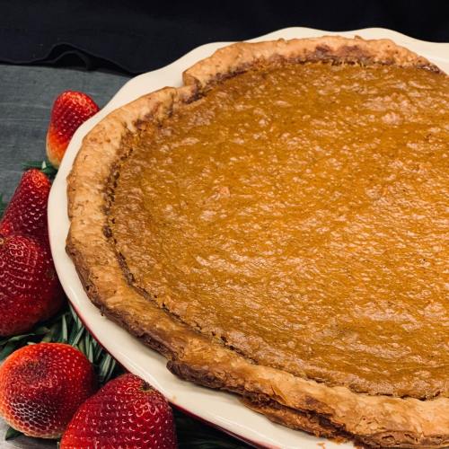 A freshly baked pumpkin pie on a white plate, surrounded by fresh strawberries.