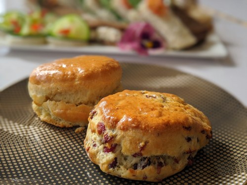 Two freshly baked scones on a patterned plate, with a colorful dish of food in the background.