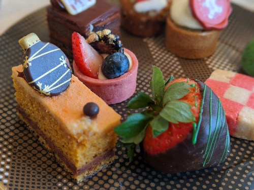 A variety of colorful desserts, including cakes, fruit tarts, and chocolate-covered strawberries on a decorative plate.