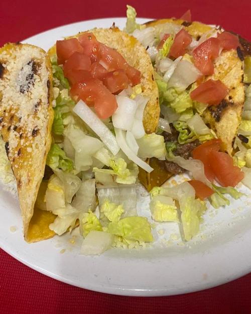 A plate of tacos topped with lettuce, diced tomatoes, and onions, served on a red tablecloth.