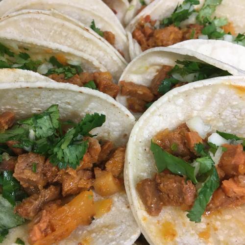 A close-up of soft tacos filled with seasoned meat, cilantro, and diced onions, arranged neatly on a plate.