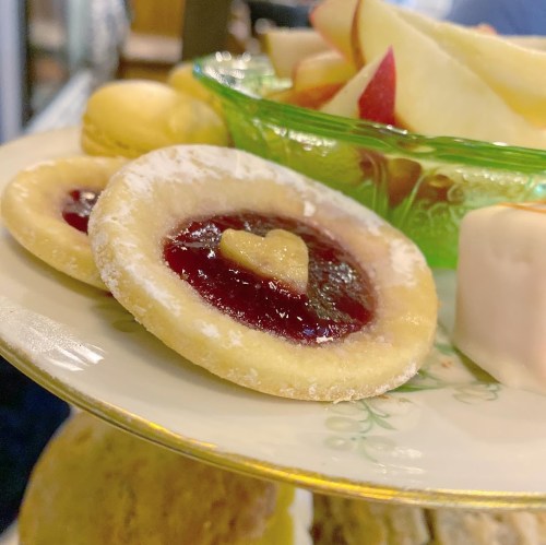A close-up of a dessert plate featuring heart-shaped jam-filled cookies and fresh apple slices.