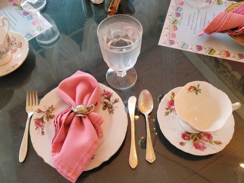 A beautifully set table with a pink napkin, floral china, silverware, and a glass of water.