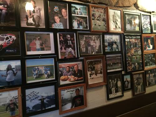 A collage of framed photographs on a wall, featuring people, sports events, and memorabilia from various occasions.