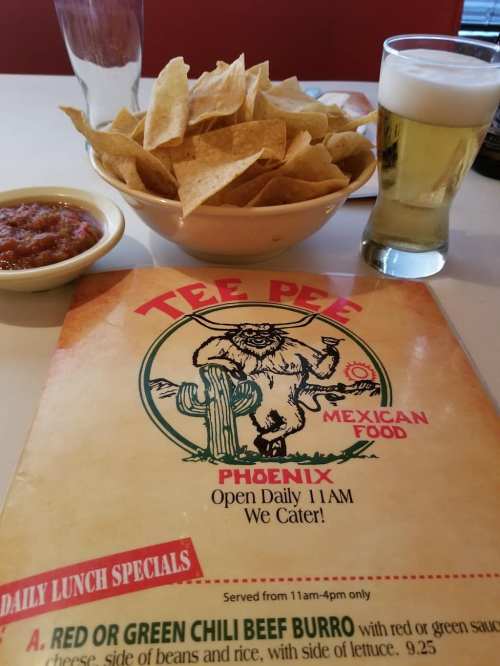 A menu for Tee Pee Mexican Food, with a bowl of tortilla chips, salsa, and a glass of beer on a table.