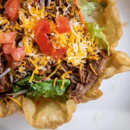 A colorful taco salad in a crispy shell, topped with shredded beef, lettuce, cheese, and diced tomatoes.