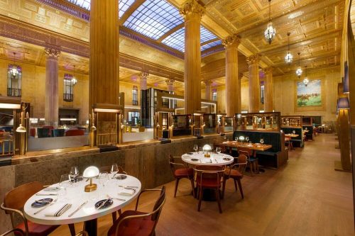 Elegant restaurant interior with tall columns, large windows, and stylish dining tables under a decorative ceiling.