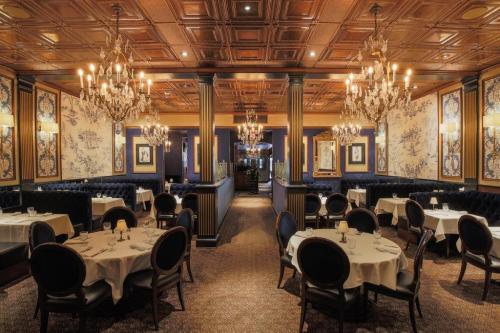 Elegant restaurant interior with chandeliers, blue velvet seating, and ornate wallpaper, featuring round tables set for dining.