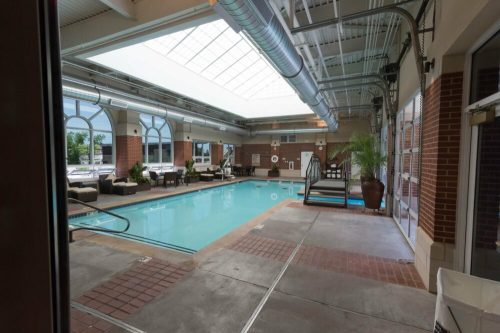 Indoor swimming pool area with a skylight, lounge chairs, and potted plants, featuring a clean, inviting atmosphere.
