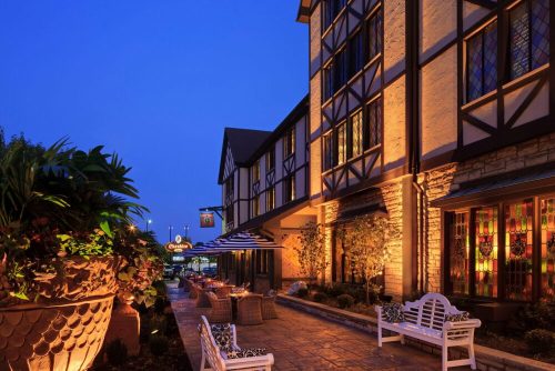 A charming restaurant exterior at dusk, featuring outdoor seating, decorative plants, and warm lighting.