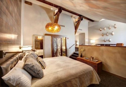 Cozy bedroom with a stylish bed, wooden beams, decorative lighting, and a staircase leading to an upper level.