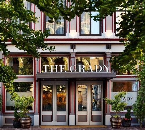 Exterior of a building named "THE GRADY," framed by greenery and featuring large windows and double doors.