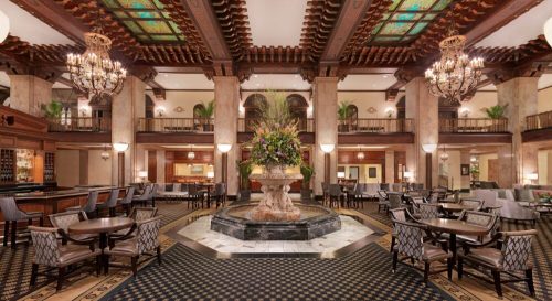 Elegant hotel lobby featuring a grand fountain, ornate chandeliers, and stylish seating areas with floral arrangements.