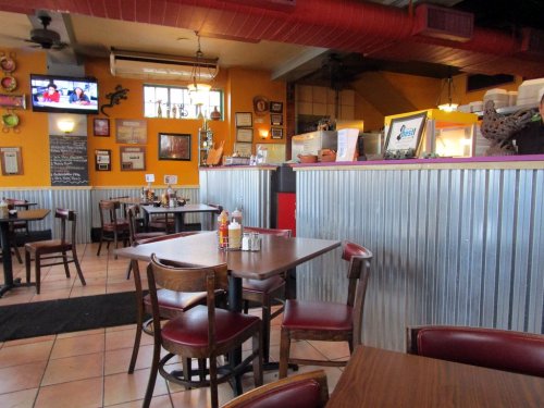 Cozy restaurant interior with wooden tables, chairs, and colorful walls, featuring a TV and decorative wall art.