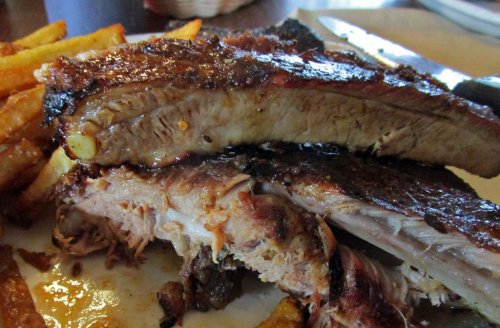 Close-up of juicy, grilled ribs served with crispy French fries on a plate.