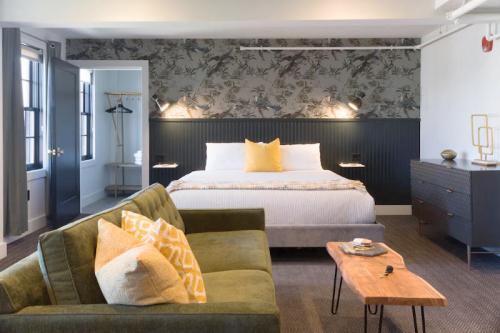 A stylish hotel room featuring a large bed, green sofa, wooden table, and floral wallpaper.
