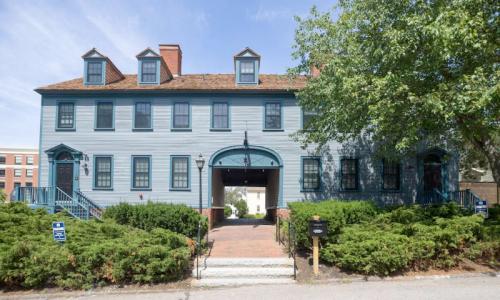 Historic blue building with multiple windows, a central archway, and greenery in front. Clear blue sky above.