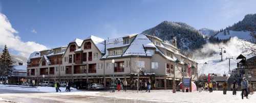 A snowy mountain resort with a building, ski lift, and people enjoying the winter scenery.